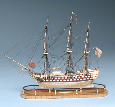   PRISONER-OF-WAR BONE MODEL OF A TRIPLE-DECKER SHIP-OF-THE-LINE, circa 1800, with seventy-eight guns run-out, carved male figurehead, engraved and polychromed stern-castle, wooden highlights, and cloth British ensigns flying at bow, masthead and stern; mounted on marquetry inlaid base. Height 19 ¾ in. Length 21 ½ in.
